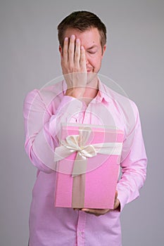 Portrait of stressed young businessman holding gift box and covering face