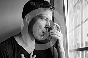 Portrait of stressed young man using asthma inhaler at home