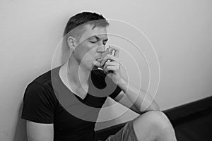 Portrait of stressed young man using asthma inhaler at home