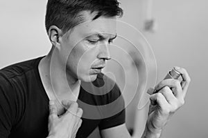 Portrait of stressed young man using asthma inhaler at home