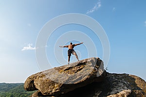Portrait of strong black bodybuilder with naked torso posing on the rock. Blue cloudy sky background