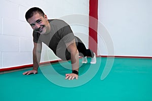 Portrait of a strong determined young man doing push-uping. He is dressed in an orange shirt and a