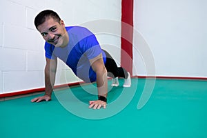 Portrait of a strong determined young man doing push-ups and looking at camera