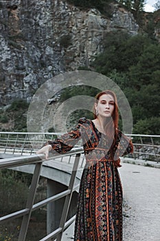 Portrait of a strong-willed strong red-haired woman in an ethnic dress near a large stone. A symbol of indomitability