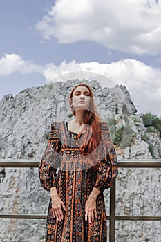 Portrait of a strong-willed strong red-haired woman in an ethnic dress near a large stone. A symbol of indomitability