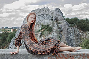 Portrait of a strong-willed strong red-haired woman in an ethnic dress near a large stone. A symbol of indomitability