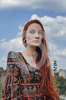 Portrait of a strong-willed strong red-haired woman in an ethnic dress near a large stone. A symbol of indomitability