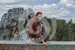 Portrait of a strong-willed strong red-haired woman in an ethnic dress near a large stone. A symbol of indomitability