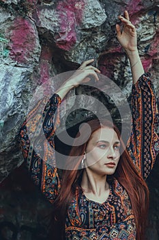 Portrait of a strong-willed strong red-haired woman in an ethnic dress near a large stone. A symbol of indomitability