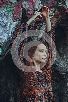 Portrait of a strong-willed strong red-haired woman in an ethnic dress near a large stone. A symbol of indomitability