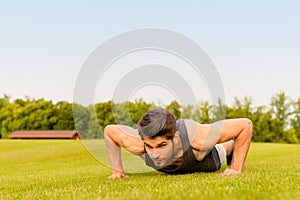 Portrait of strong young athlete push-uping in the park