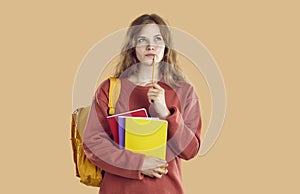 Portrait of student girl is searching for idea holding pencil near mouth on beige background.