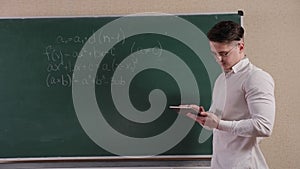 Portrait of a student in glasses with a tablet in his hands near the blackboard.