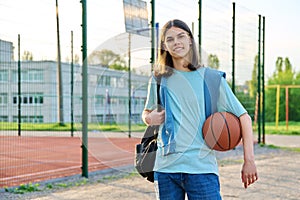 Portrait of student guy with backpack ball, near outdoor basketball playground