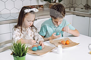 Portrait of studiously joyful two little kids boy and girl, painting brush coloring Easter eggs. Family holiday tradion