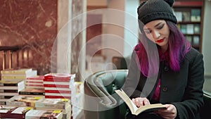 Portrait of stunning asian woman with bright red lips and purple hair reading a book in a bookstore. Concept of hipster