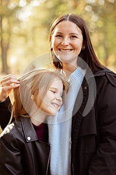 Portrait of stunning beautiful family of young woman and teenage girl standing, embracing in forest park in autumn.
