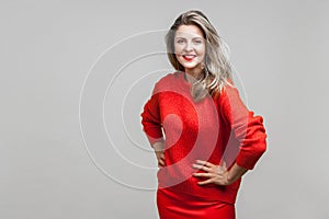 Portrait of stunning happy blonde woman with red lipstick in bright casual sweater, isolated on gray background