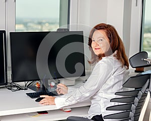 Portrait of stylish adult 60s year old woman sitting at the computer in the office, businesswoman .