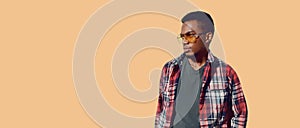 Portrait of stylish african man wearing sunglasses, red plaid shirt, guy looking away isolated on brown background, blank copy