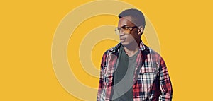 Portrait of stylish african man wearing sunglasses, red plaid shirt, guy looking away isolated on yellow background, blank copy