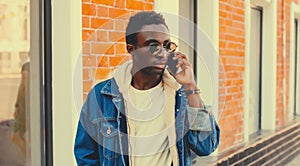 Portrait of stylish african young man talking on phone while walking on city street