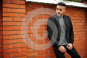 Portrait of stylish arab beard man wear grey turtleneck and black jaket. Arabian model guy against brick wall