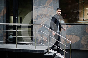 Portrait of stylish arab beard man wear grey turtleneck and black jaket. Arabian model guy walking down stairs