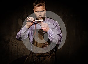 Portrait of stylish barber with beard and professional tools on a dark background.