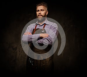 Portrait of stylish barber with beard and professional tools on a dark background.