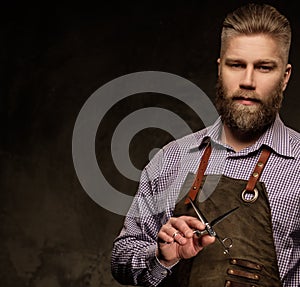 Portrait of stylish barber with beard and professional tools on a dark background.