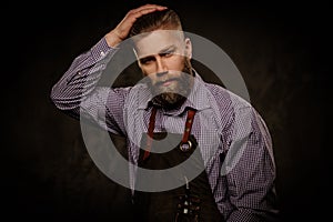 Portrait of stylish barber with beard and professional tools isolated on a dark background.
