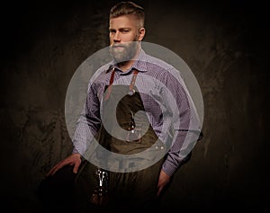 Portrait of stylish barber with beard and professional tools isolated on a dark background.