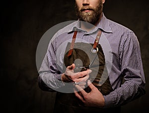 Portrait of stylish barber with beard and professional tools isolated on a dark background.