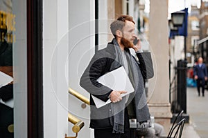 Portrait of a stylish bearded business man with a laptop in his hands talking on the smartphone