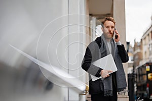 Portrait of a stylish bearded business man with a laptop in his hands talking on the smartphone.