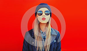 Portrait of stylish beautiful blonde woman blowing her red lips sending sweet air kiss wearing round sunglasses, black rock style