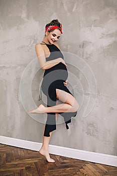 Portrait of the stylish beautiful pregnant woman with big belly and long legs in black long summer dress, future mother