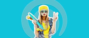 Portrait of stylish blonde young woman model with skateboard wearing colorful yellow hat on blue background, magazine style