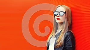 Portrait of stylish blonde young woman posing wearing sunglasses in the city on red background