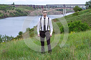 Portrait of stylish brunet young man, wearing white shirt, black tie, suspenders and sunglasses