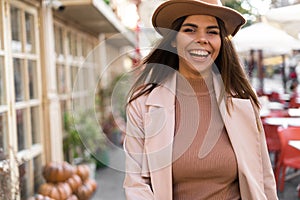 Portrait of a stylish cheerful Caucasian woman with loose long hair in a coat and hat near a cafe in the city. Fashion.
