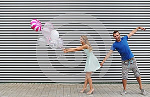 Portrait of stylish couple holding colorfull balloons, on striped wall background