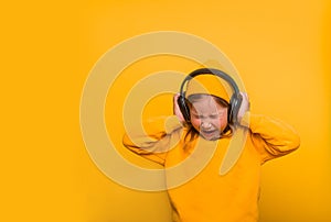 Portrait of stylish cute little kid girl listening music in headphones and singing against pink background. School child