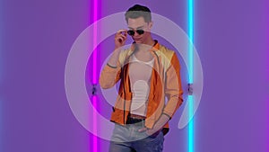 Portrait of stylish guy playfully looking at the camera in sunglasses. Male fashion model in yellow jacket poses in dark