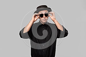 Portrait of a man in a black shirt, pork pie and sun glasses hat isolated over grey background.