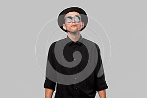 Portrait of a man in a black shirt, pork pie and sun glasses hat isolated over grey background.