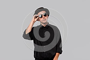 Portrait of a man in a black shirt, pork pie and sun glasses hat isolated over grey background.