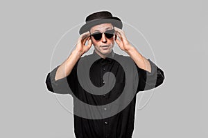 Portrait of a man in a black shirt, pork pie and sun glasses hat isolated over grey background.