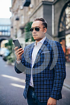 Portrait of stylish handsome young man with bristle standing outdoors. Man wearing jacket and shirt. man using mobile phone